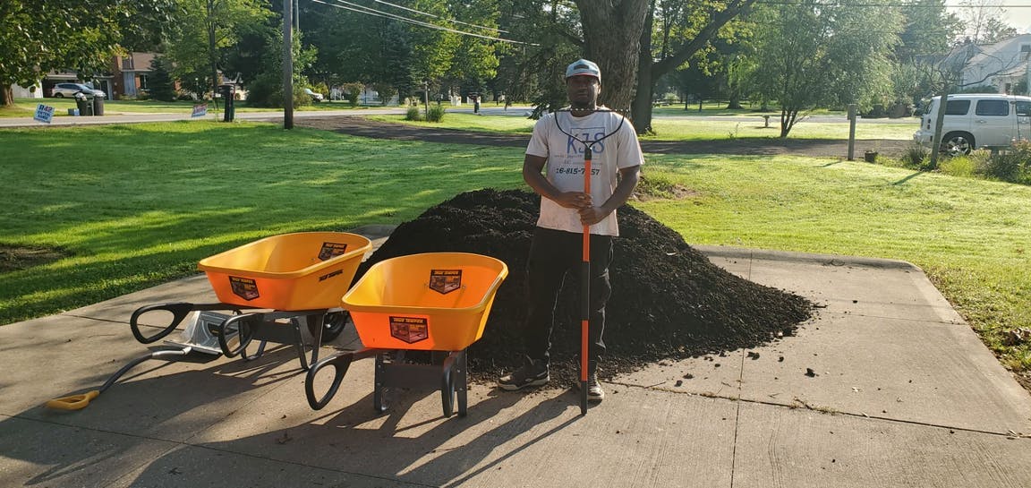 Mulching service about to begin in Willowick, Ohio as an employee at Kevin J Services stands by a pile of mulch and 2 wheel barrels
